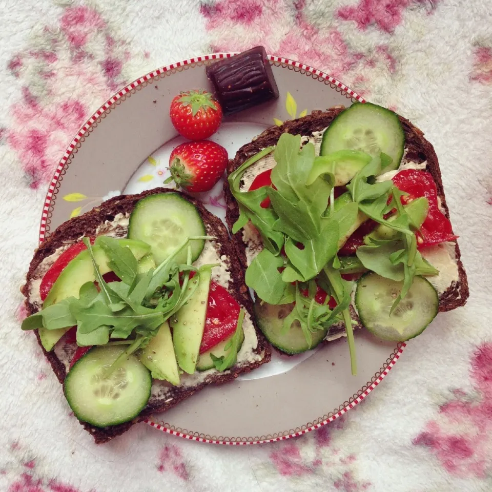 Whole grain toast with hummus, tomatoes, cucumber, avocado and arugula. Strawberries and raw vanilla mulberry chocolate piece on the side|Rianneさん