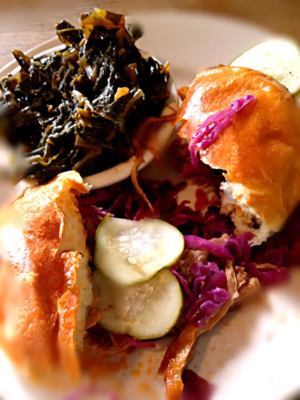 Pulled pork sandwich on a brioche bun with purple cabbage slaw and dill pickle slices, served with sweet collared greens.|Meg Davisさん