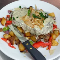 20 oz ribeye served under a bed of fried potatoes and roasted veggies top with a garlic sauce|Steven Doportoさん