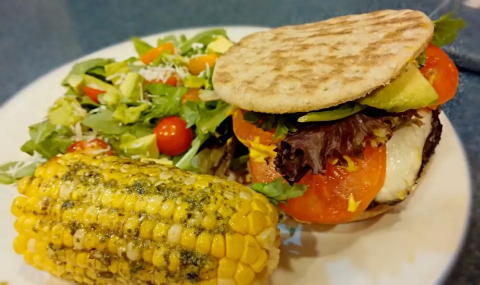 lamb burger stuffed with mozzarella topped with queso blanco with sides of arugula salad and grilled corn spread with basil pesto.|Jiraphon Gさん