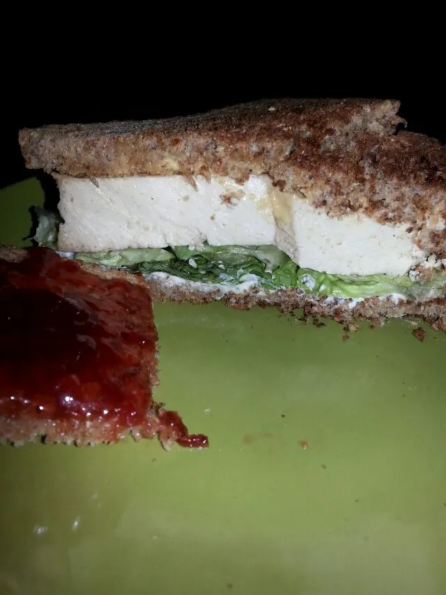 marinated tofu sandwich with lettuce and cream chz on Ezekiel bread.  with a slice of bread with butter and strawberry preserves as dessert.|Polly Gelfusoさん