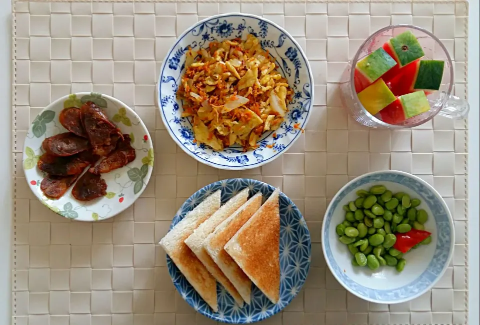 Breakfast: sausage, fried egg with carrot, toast, green soy bean, watermelon stick.|Liciaさん