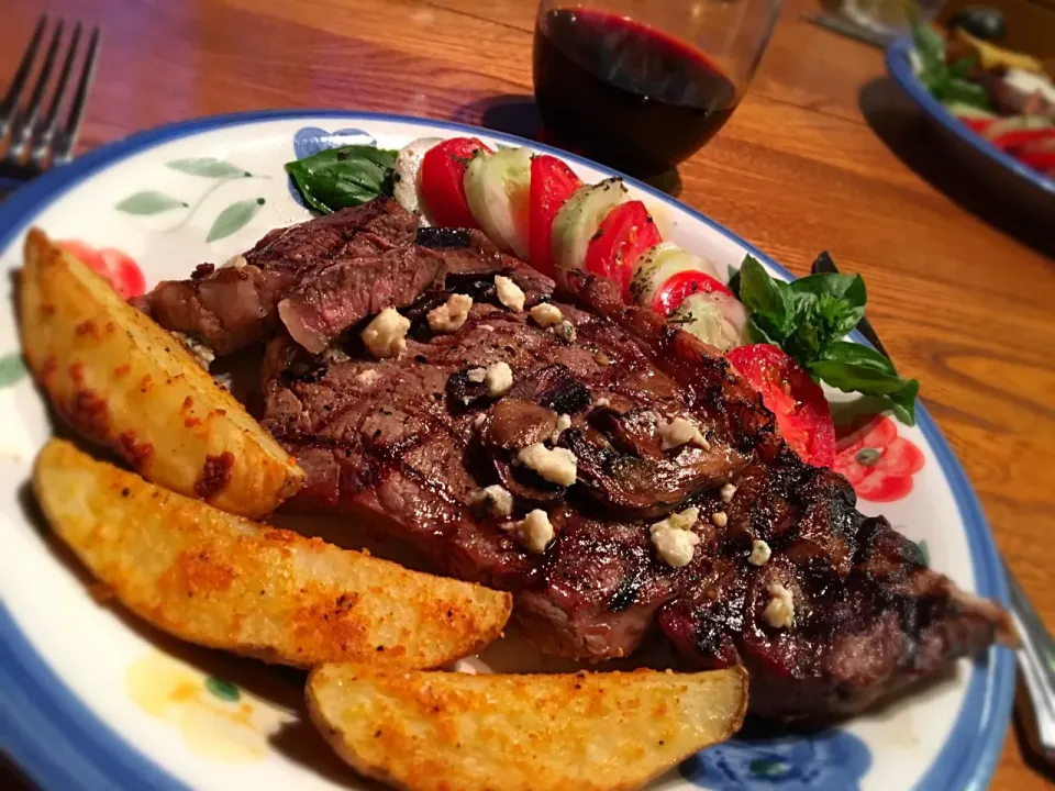 Perfectly grilled ribeye steaks topped with mushrooms and blue cheese; baked garlic/Parm potato wedges and garden fresh tomato/cucumber salad.|MJRoperさん