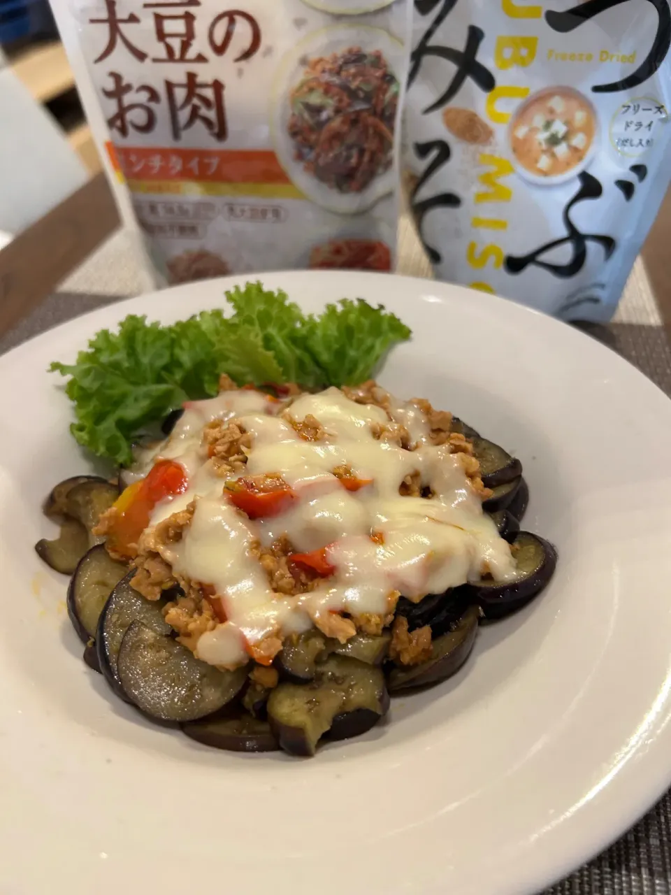 ナスの肉味噌チーズ焼き♪大豆のお肉ミンチはオリーブオイルでさっと炒め鶏がらスープ、粒味噌、トマト、きざみ生姜を入れてさっと煮込みます。レンチンしたナスのスライスの上に大豆のお肉ミンチを盛りチーズをかけてチーズがとろけるまでレンチンしたら出来上がり♪|笙　みかんさん